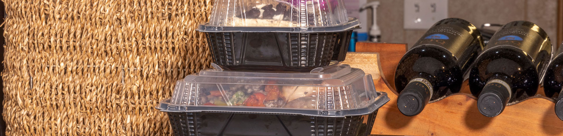 hinged food containers filled and ready for pick up next to wine bottles