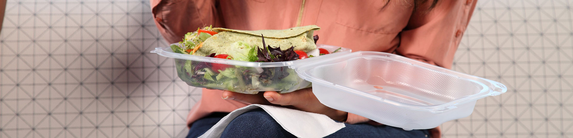 lap of person eating salad from clear hinged food container